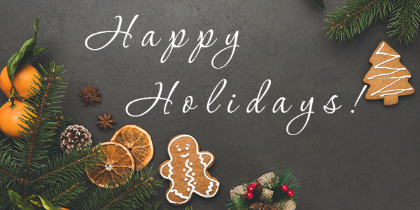 Image of holiday decorations, ginger bread cookies, oranges and orange slices, pine tree branches, pine tree seed, star anise, and a clothes wrappe present laid on a dark grey stone background; Happy Holidays!