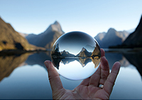 Image of person holding up glass ball in front of lake and mountains