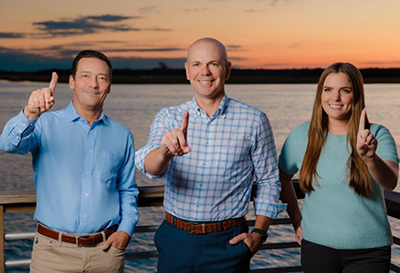 Sam Catlett, Todd Godin, and Adrieanna Piantedosi holding up one finger standing in front of a beautiful sunset