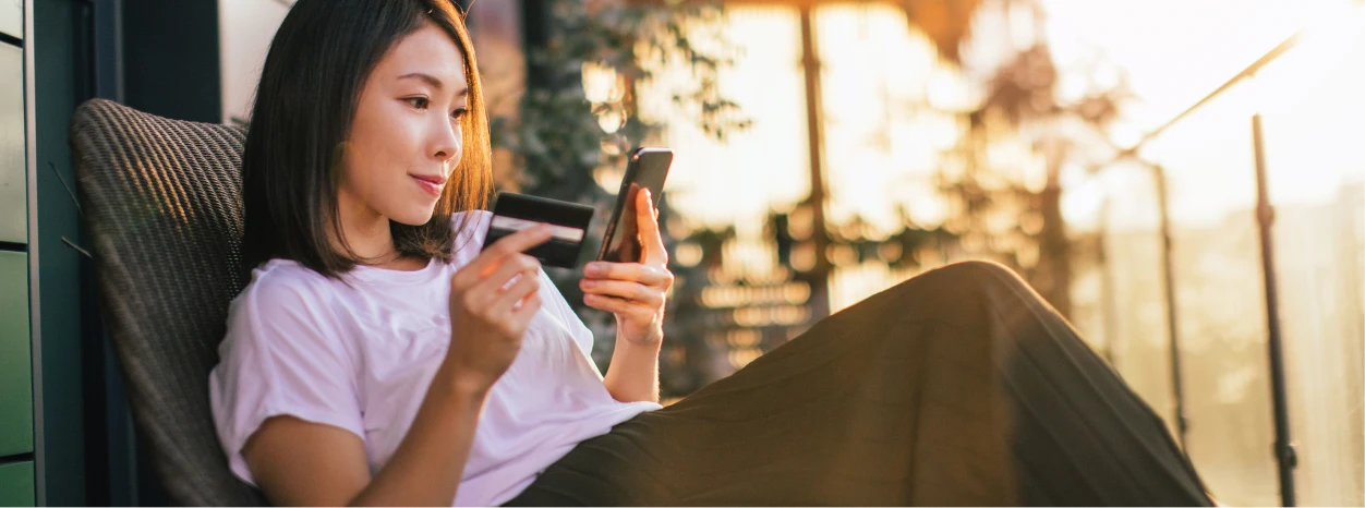Woman outside looking at her phone while holding a credit card